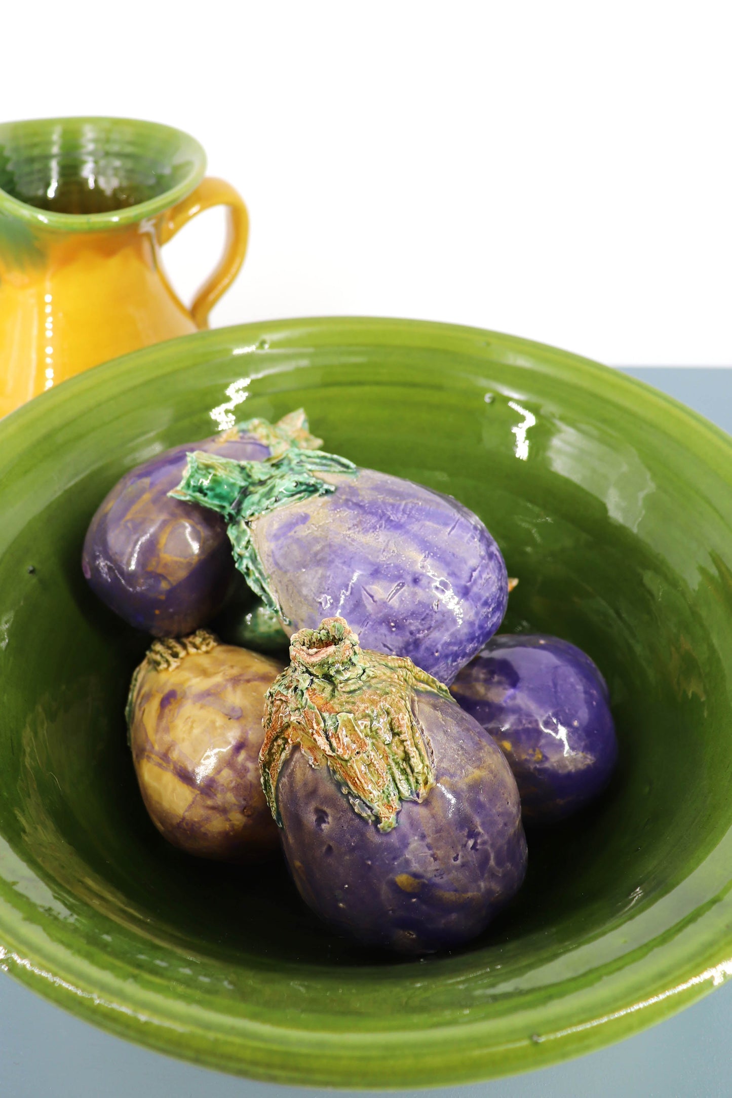 Bowl verde con berenjenas moradas decorativas, cerámica artesanal, estilo rústico y colorido.