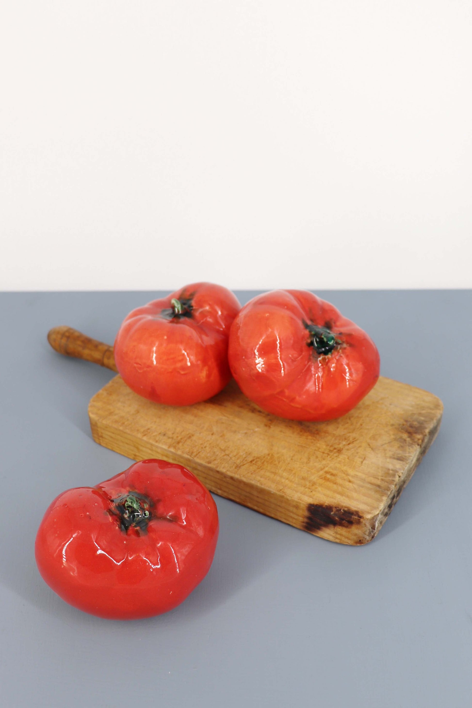 Conjunto de tomates rojos de cerámica brillante sobre una tabla de madera natural, estilo rústico para decoración.