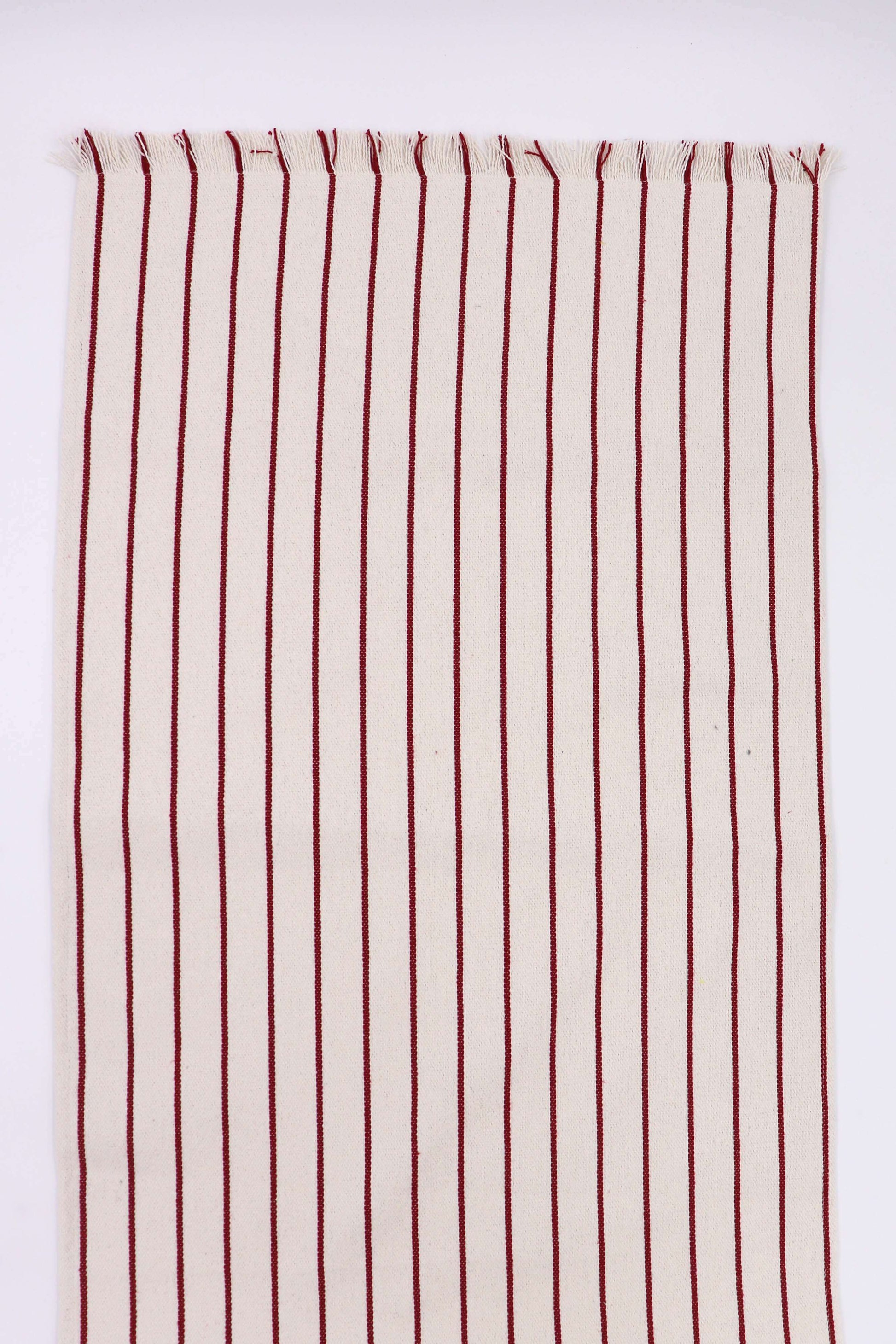 Camino de mesa granate con rayas verticales sobre fondo claro, tejido artesanal con flecos