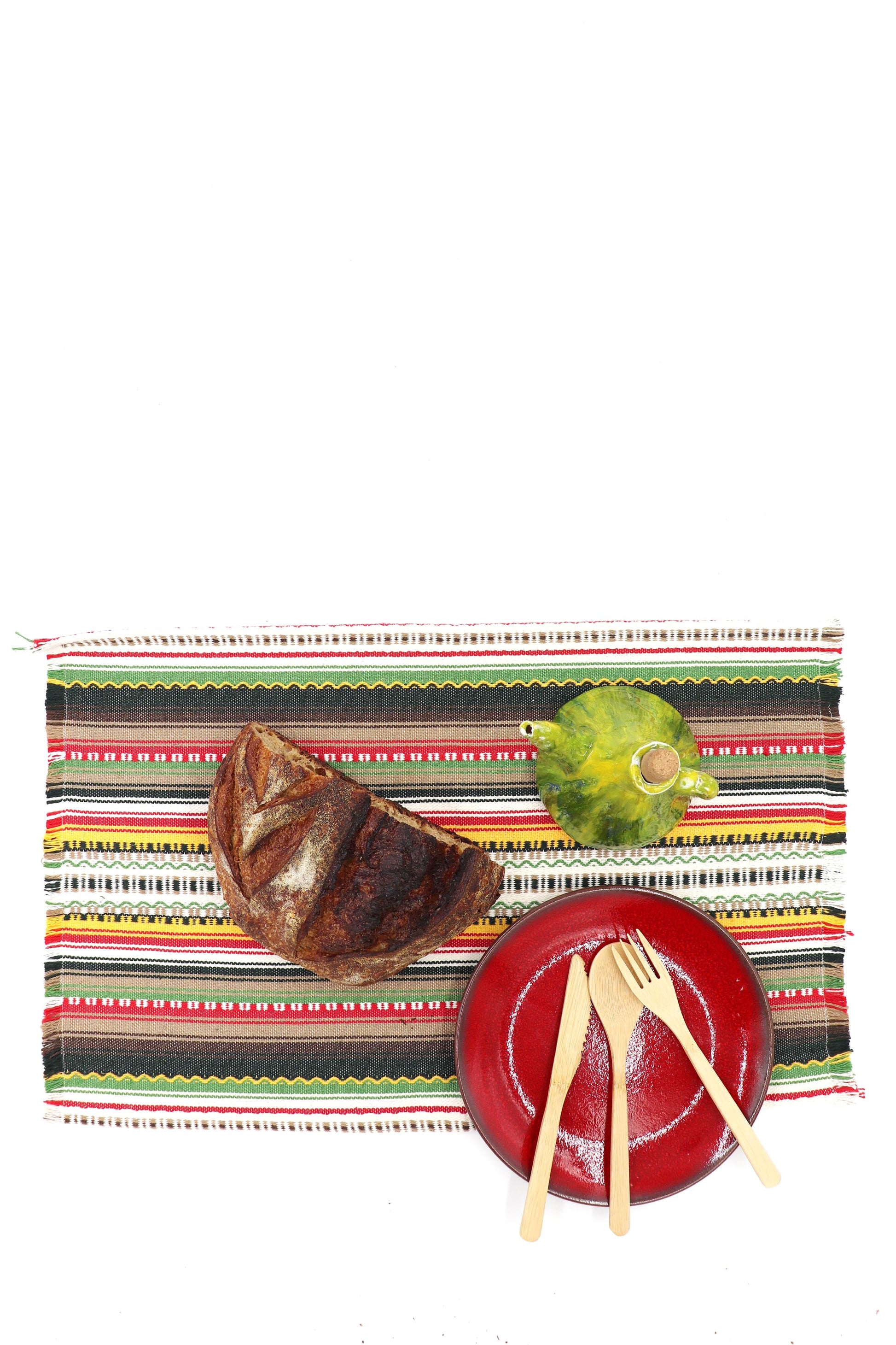 Mantel de rayas rojas y verdes con plato rojo, utensilios de madera y un jarrón verde. Ideal para comidas al aire libre.