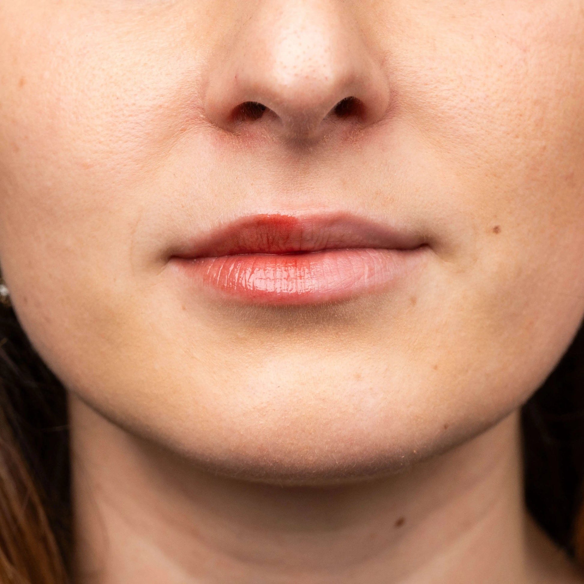 Close-up of lips with a glossy raspberry-colored tint applied to the left side, showing a hydrating, natural finish.