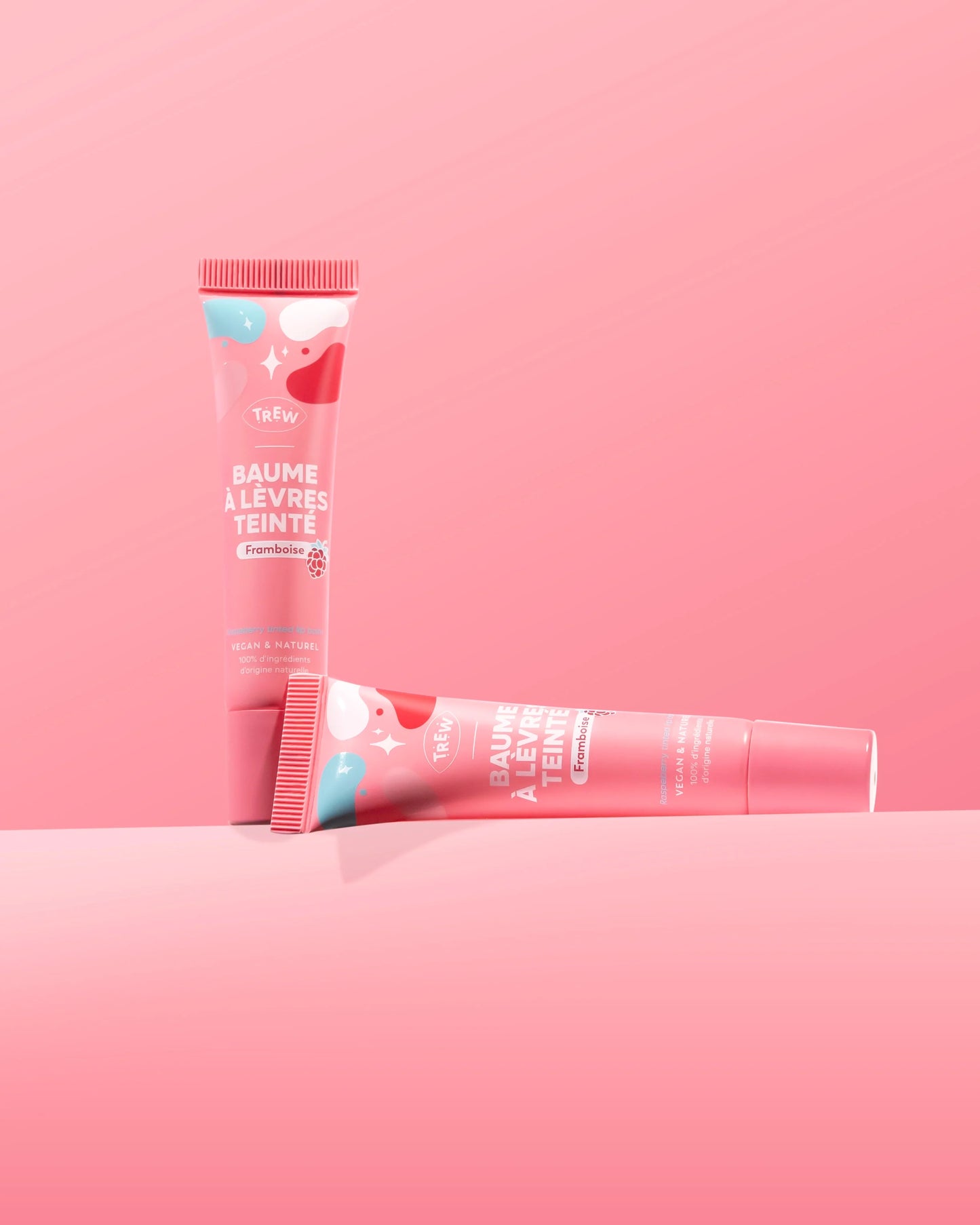 Two pink tubes of raspberry tinted lip balm with white abstract patterns, one standing upright, one lying horizontally.