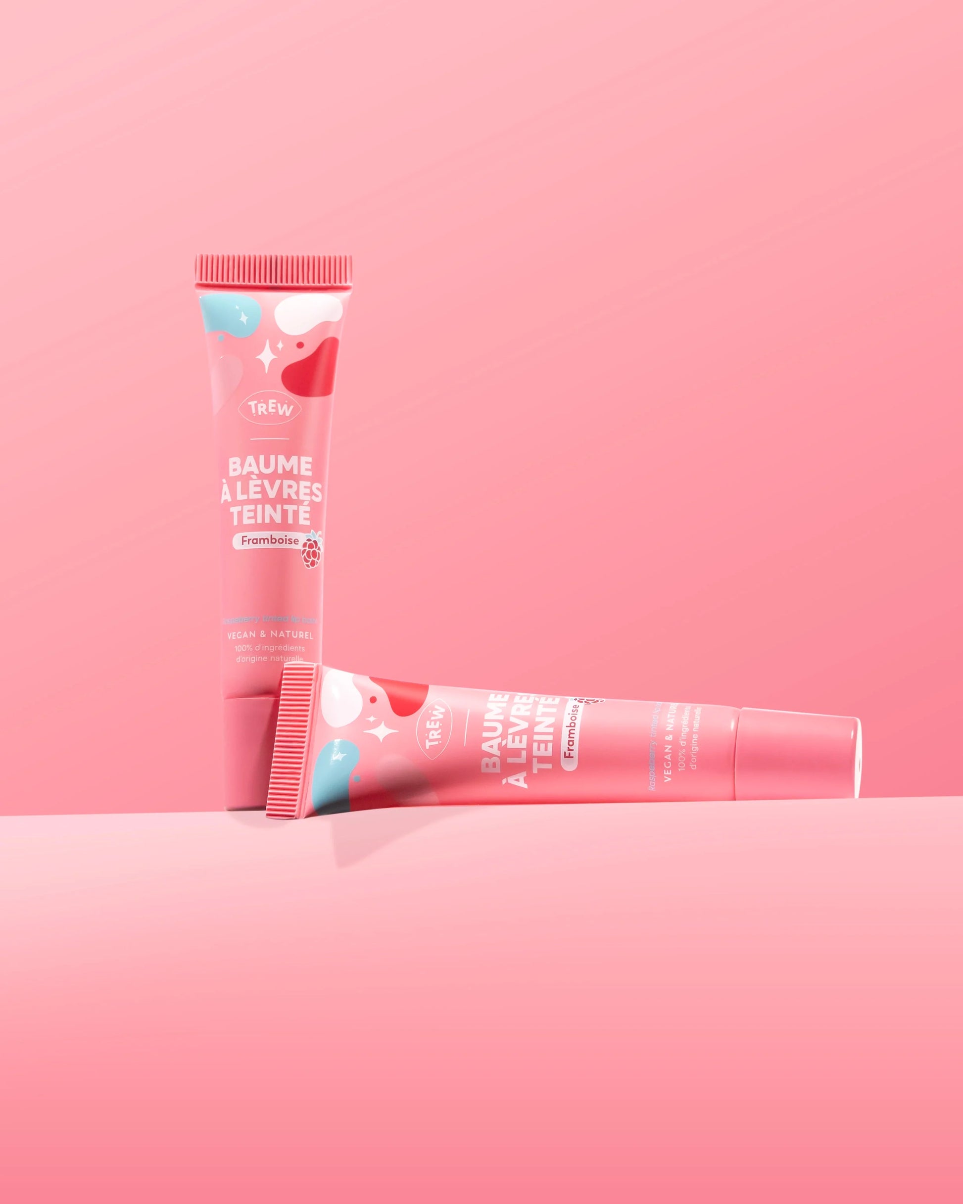Two pink tubes of raspberry tinted lip balm with white abstract patterns, one standing upright, one lying horizontally.