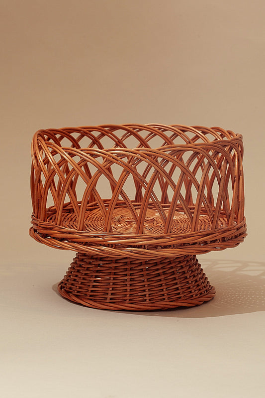 Round pedestal fruit bowl made of natural woven wicker with an openwork lattice design in a warm tan color.