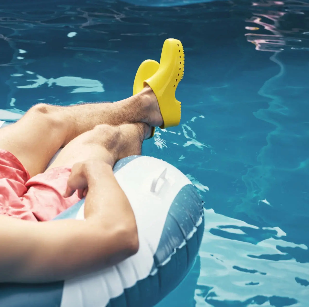 Bright yellow, solid-style rubber clogs worn by a person relaxing on a pool float in blue water.