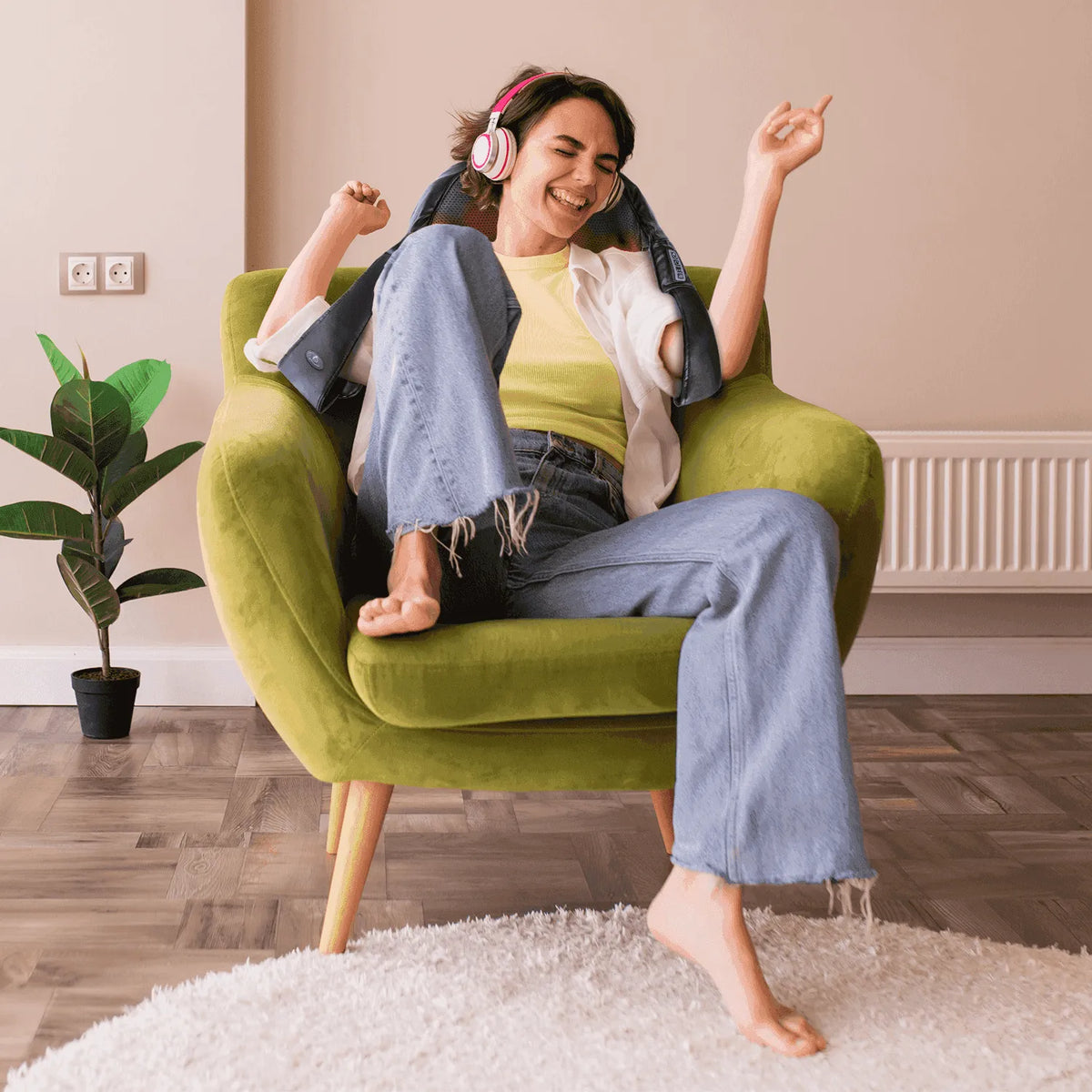 Woman wearing a black 3D Shiatsu neck and shoulder massager with glowing red heat nodes while sitting in a green chair.