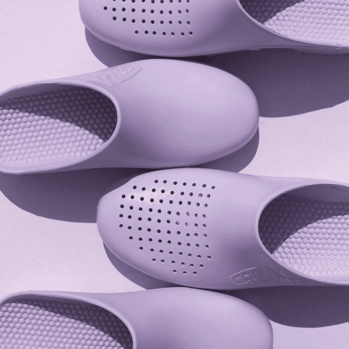 Lavender-colored rubber clogs with air holes, textured insoles, and a round-toe, slip-on design on a white background.