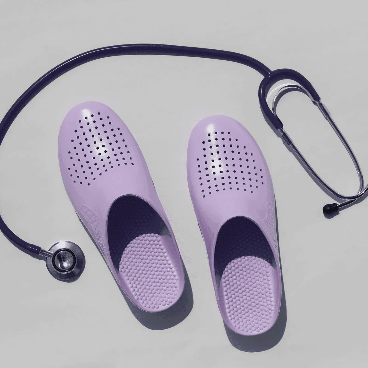 Lavender rubber clogs with ventilation holes and a textured sole, paired with a purple medical stethoscope.