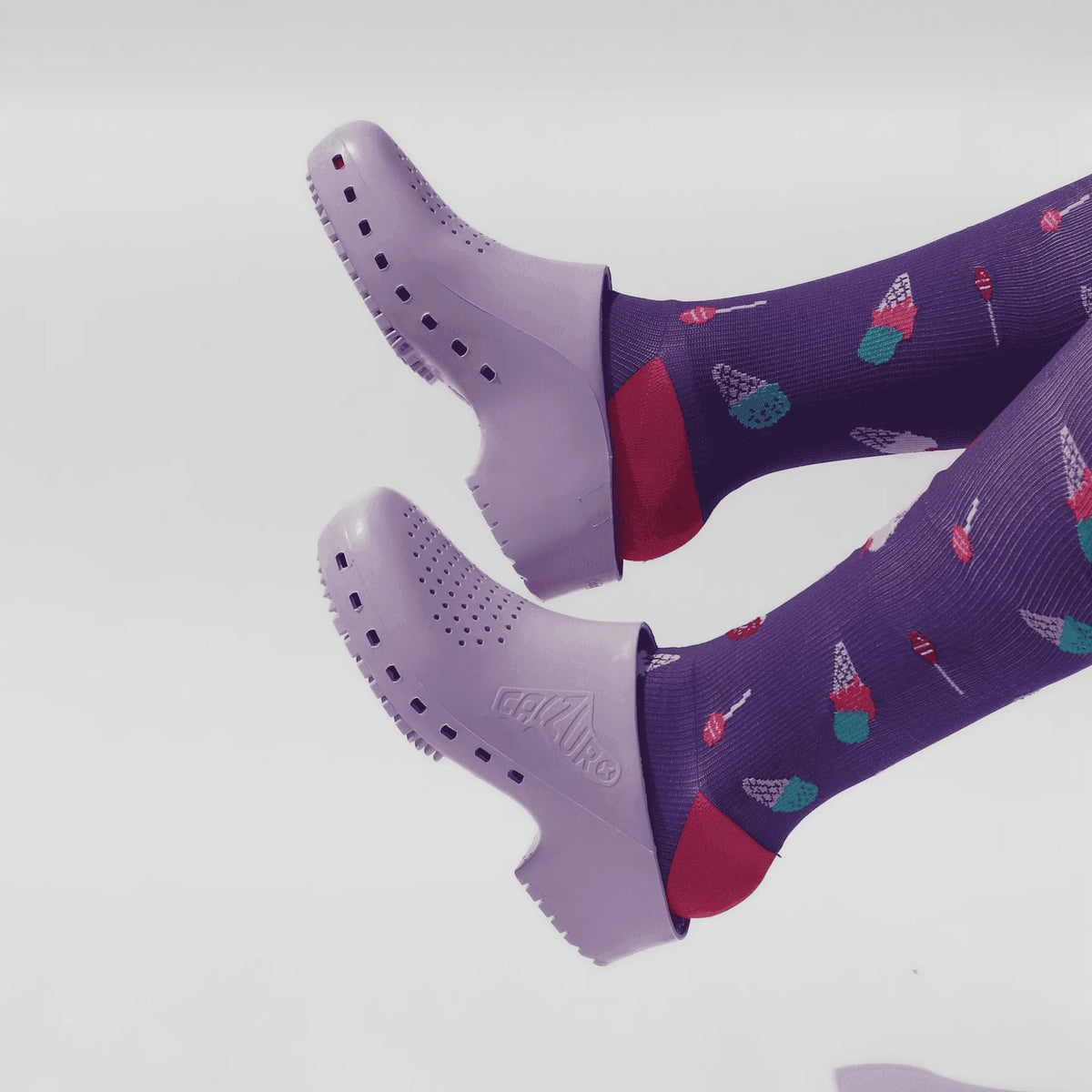 Lavender rubber clogs with side ventilation holes worn over purple socks with an ice cream cone pattern.
