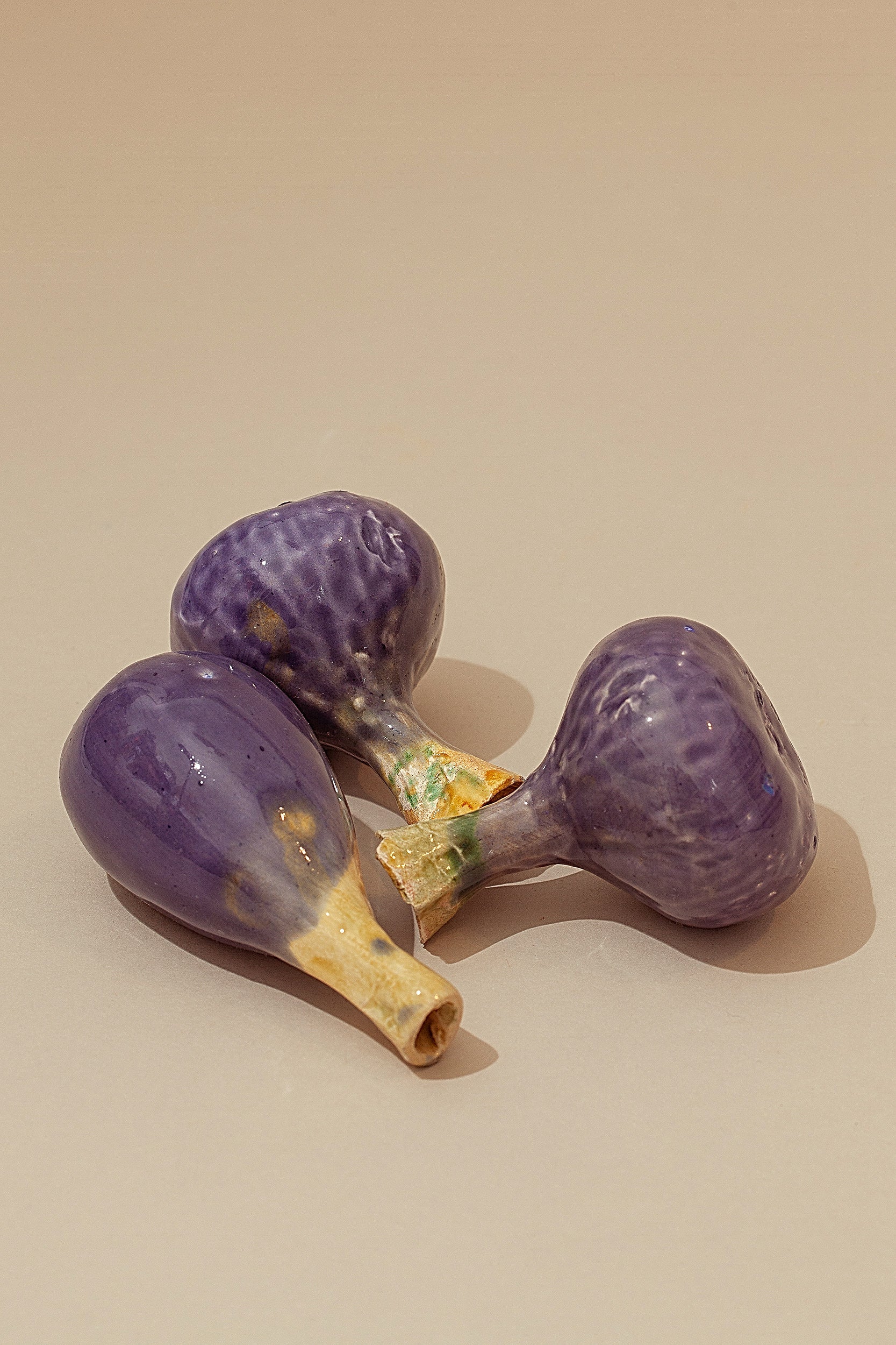 Figuras decorativas de cerámica en forma de higos morados, con detalles en tonos crema y verdes.