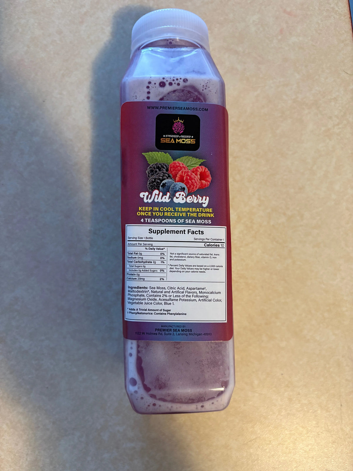 12 oz. square plastic bottle of purple Wild Berry sea moss lemonade with a label featuring berry illustrations.