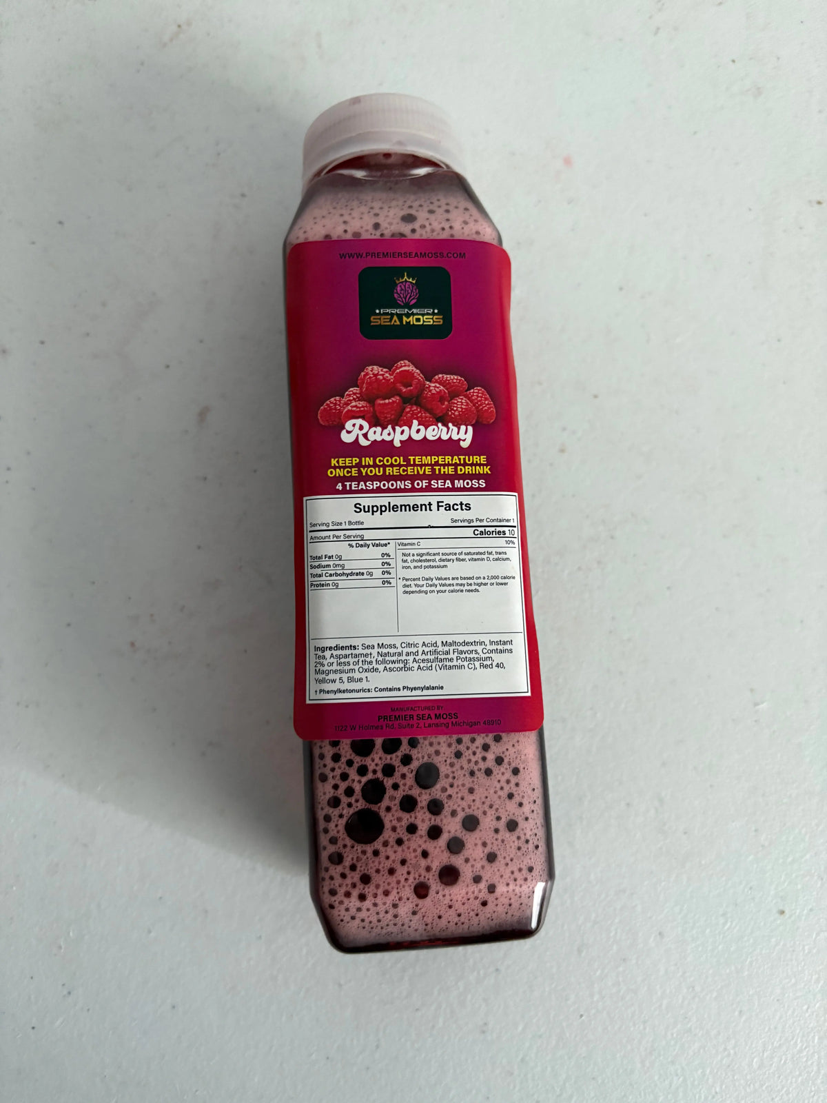 12 oz. bottle of raspberry sea moss lemonade with a pink label featuring raspberries and supplement facts.
