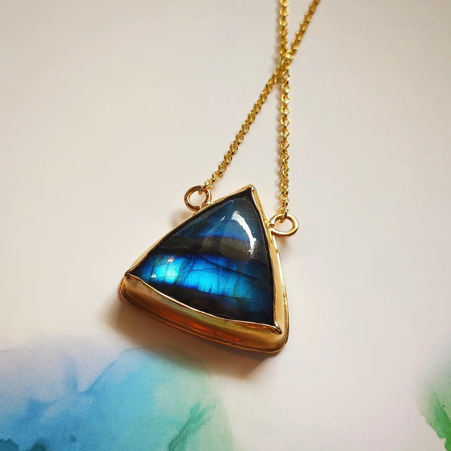 Collar de triángulo dorado con piedra labradorita azul, diseño elegante y moderno.