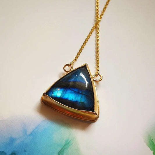 Collar de triángulo dorado con piedra labradorita azul, diseño elegante y moderno.