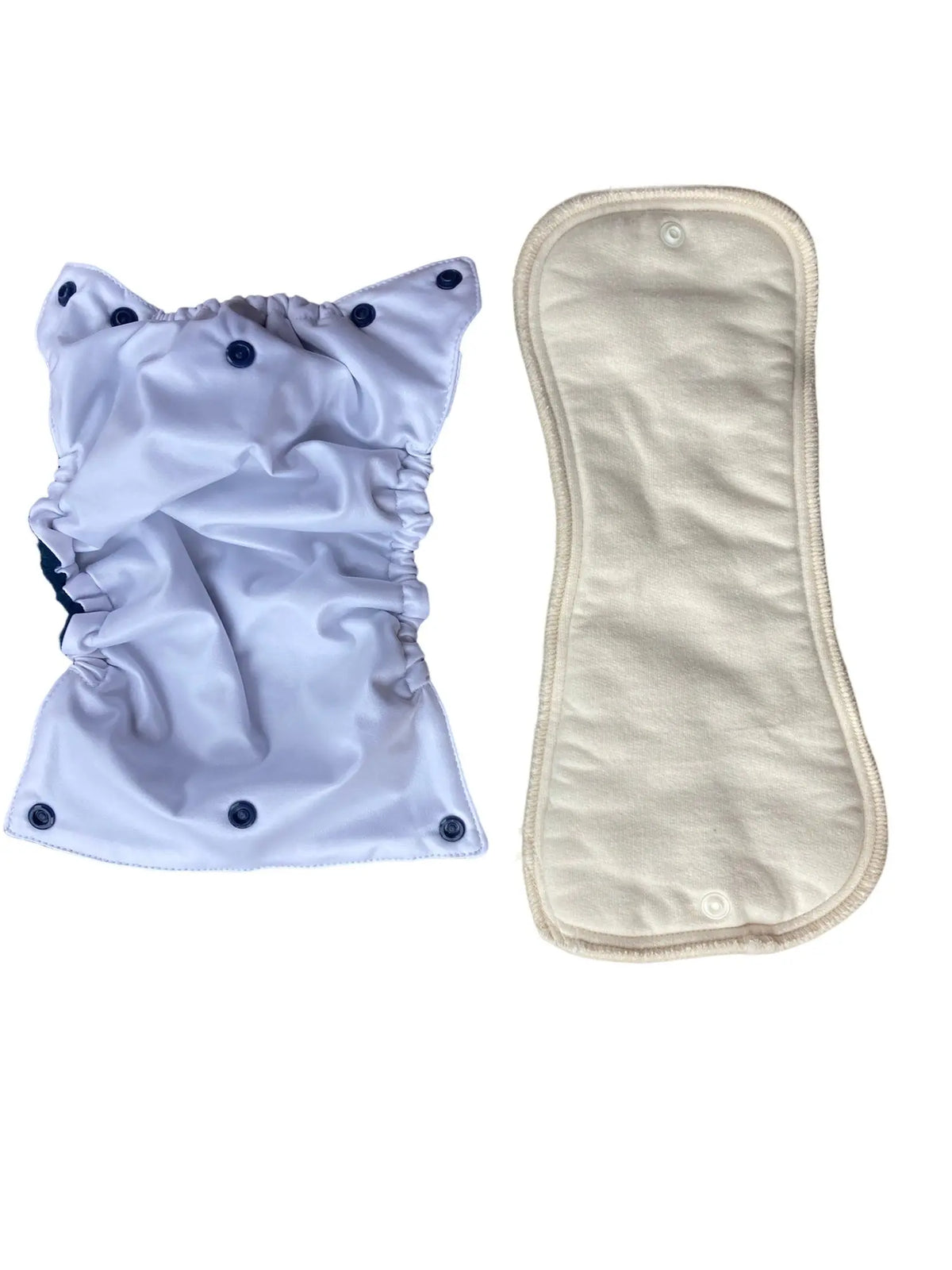 A white diaper cover with dark blue snaps next to an hourglass-shaped, cream-colored absorbent fabric snap-in pad.