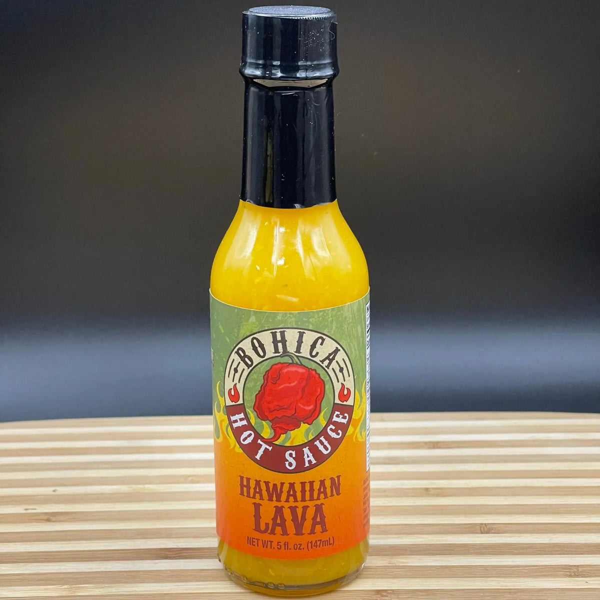 A bottle of Hawaiian Lava hot sauce with vibrant yellow liquid, a black cap, and a label featuring a red pepper.