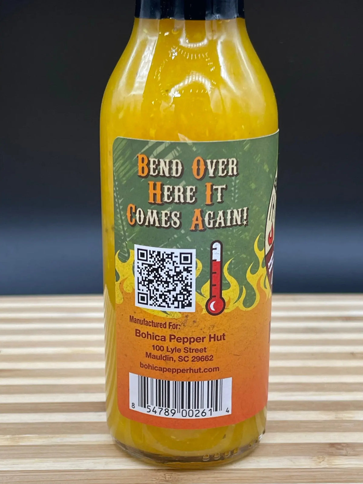 A bottle of bright yellow Hawaiian Lava hot sauce with a green and orange label featuring a QR code and thermometer.