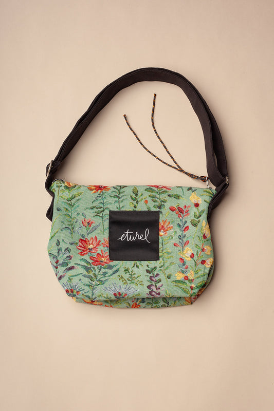 Bolso bandolera de jacquard celeste con estampado de flores coloridas, correa negra ajustable y cierre de cremallera.