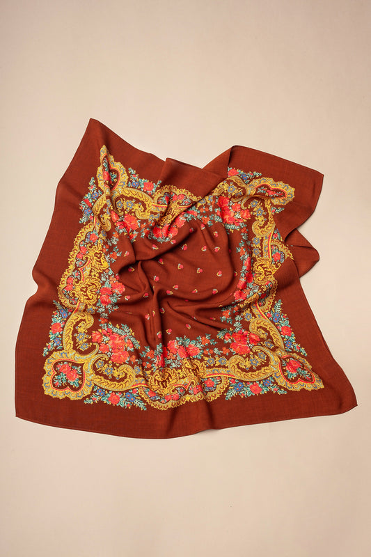 Pañuelo color mocca con estampado floral tradicional, bordes ornamentados en tonos dorados, rojos y azules sobre fondo liso.