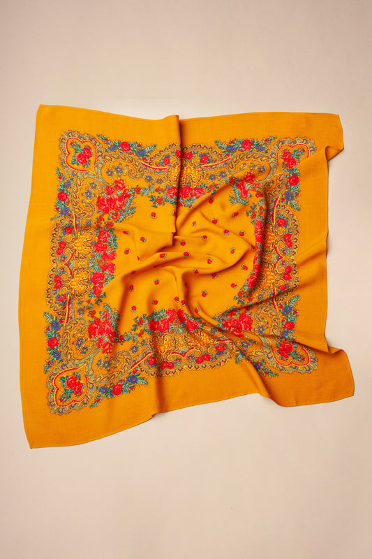 Pañuelo cuadrado ocre con estampado tradicional de flores rojas y motivos de cadenas en tonos azules y dorados.