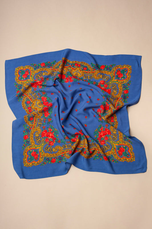 Pañuelo azul con estampado tradicional de flores rojas y bordes ornamentados en tonos dorados sobre fondo beige.