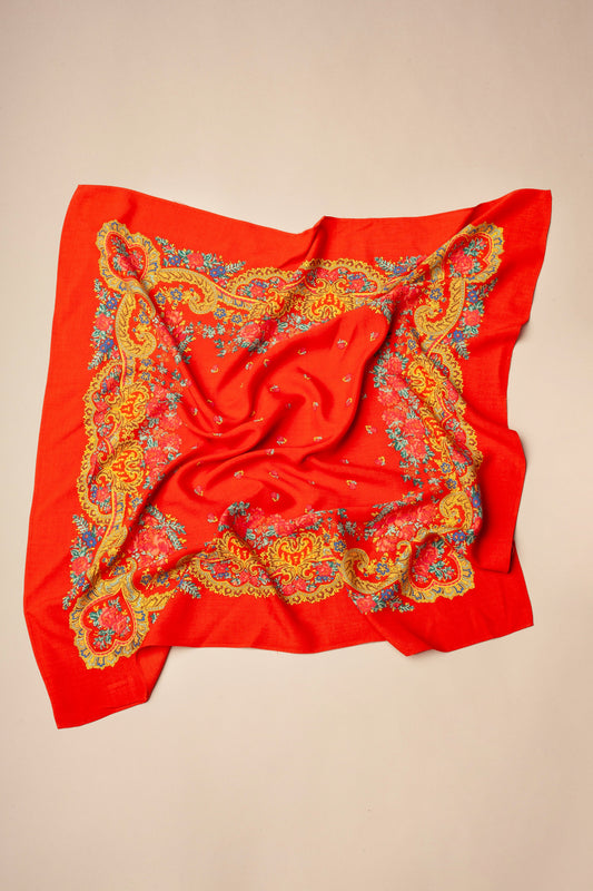Square red scarf with yellow, blue, and pink floral chain-link border patterns on a neutral beige background.