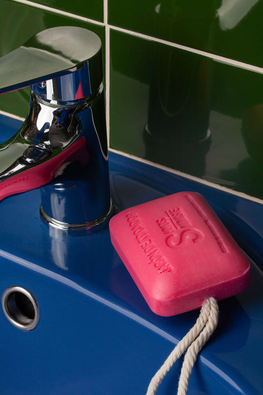 Pastilla de jabón rosa con cuerda sobre lavabo azul brillante junto a grifo cromado y azulejos verdes de pared.