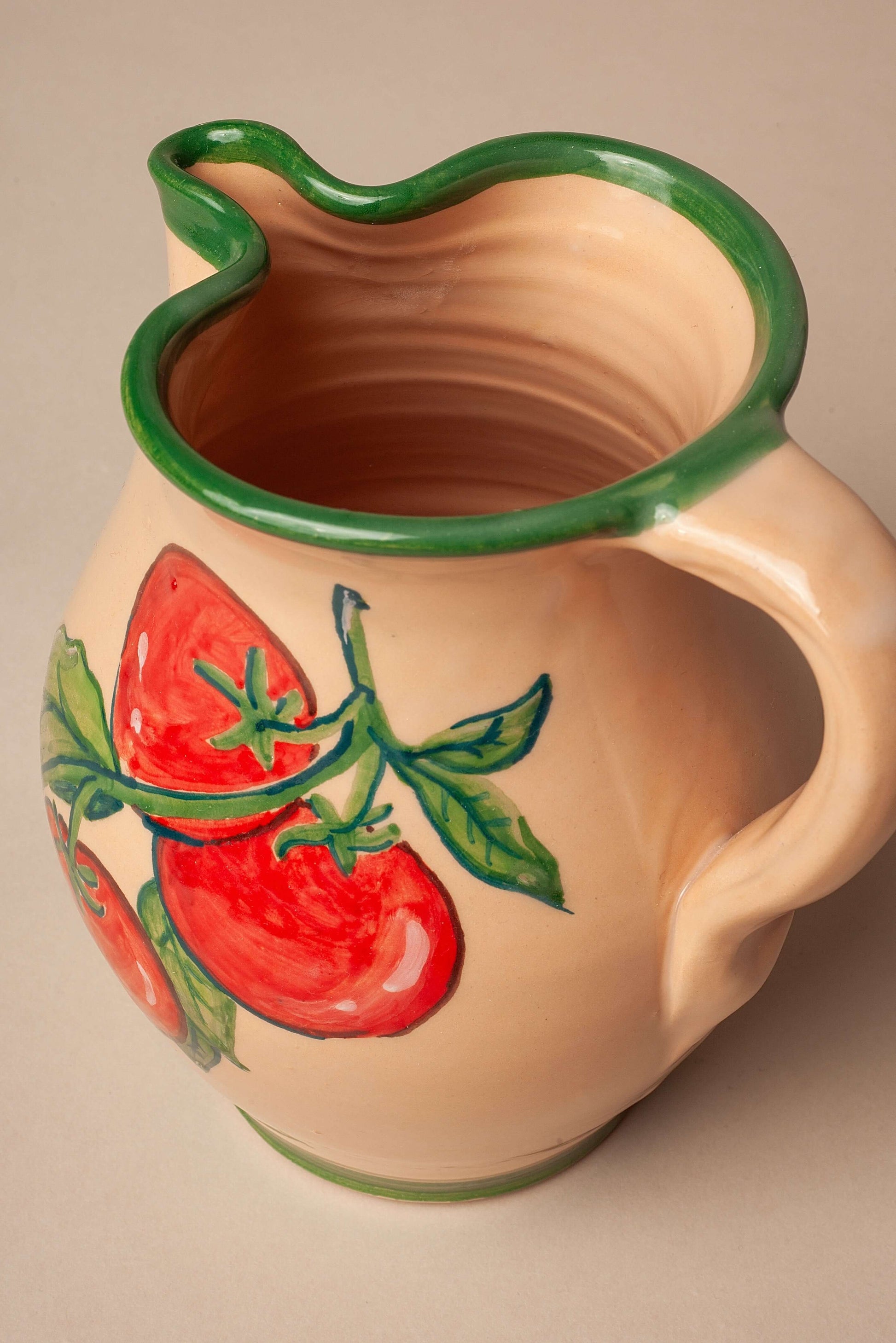 Jarra de cerámica artesanal color crema con borde verde y dibujo pintado a mano de tomates rojos con hojas verdes.