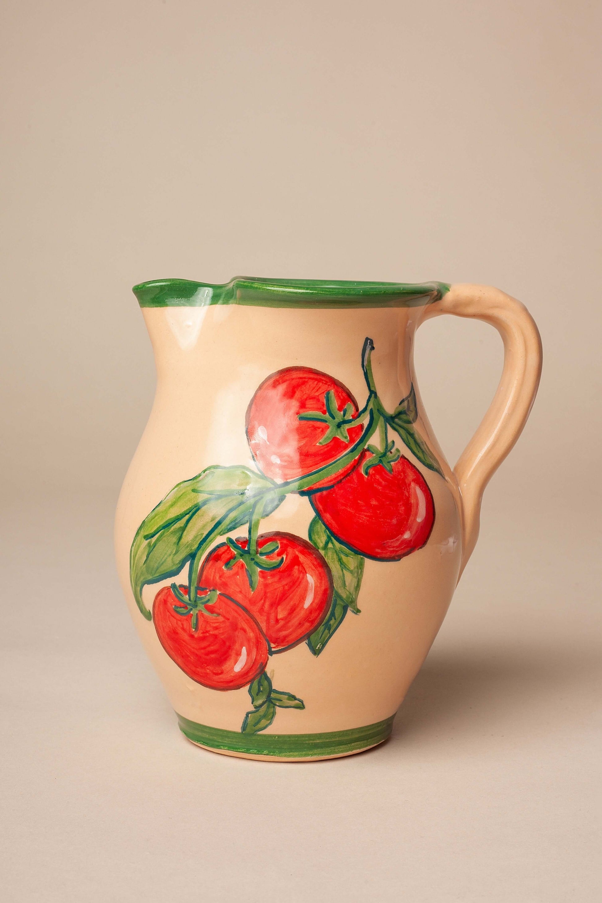 Jarra de cerámica color crema con diseño artesanal pintado a mano de tomates rojos y hojas verdes sobre fondo neutro.