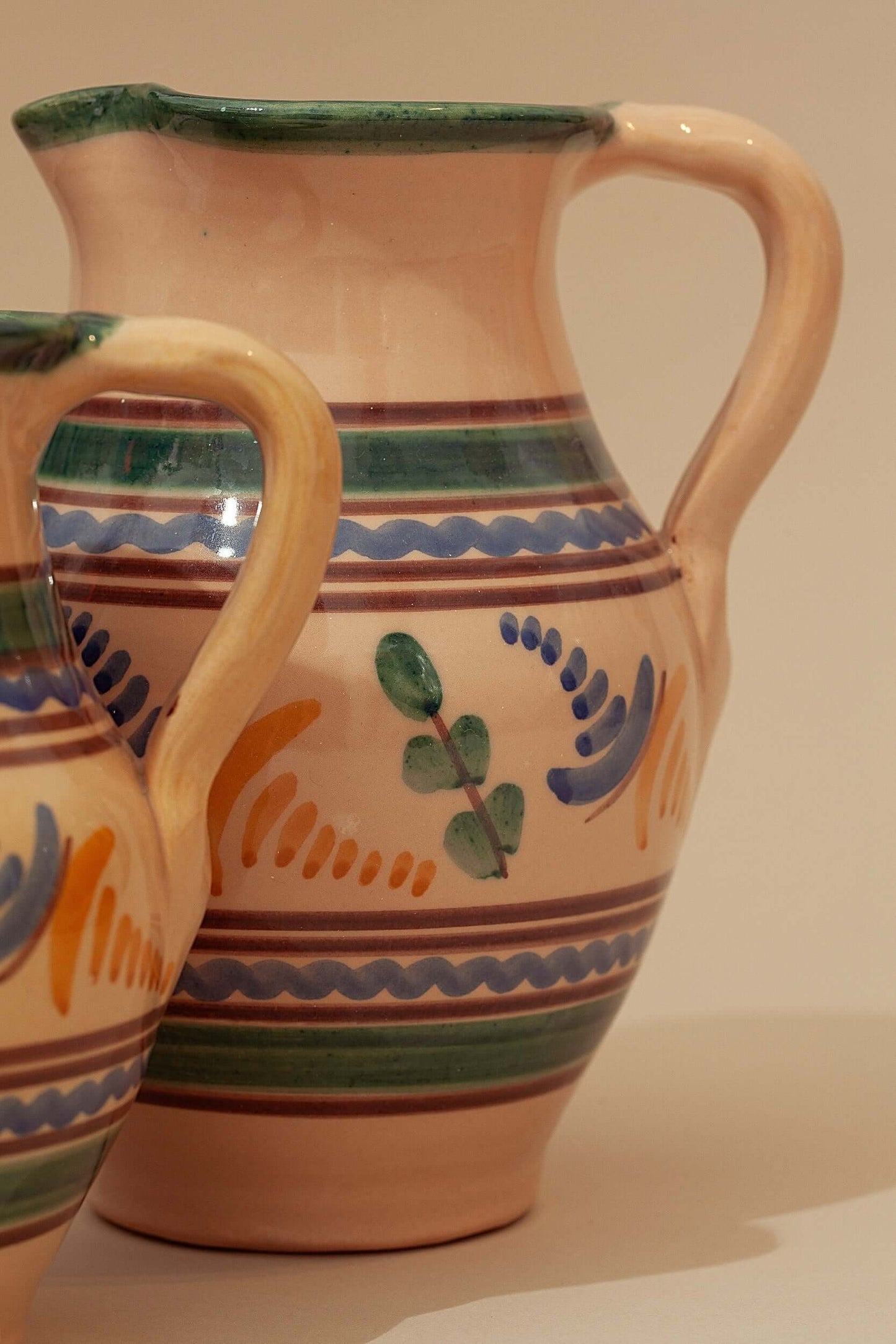 Jarras de cerámica artesanal con motivos florales pintados a mano en tonos verdes, azules y ocres sobre fondo crema.