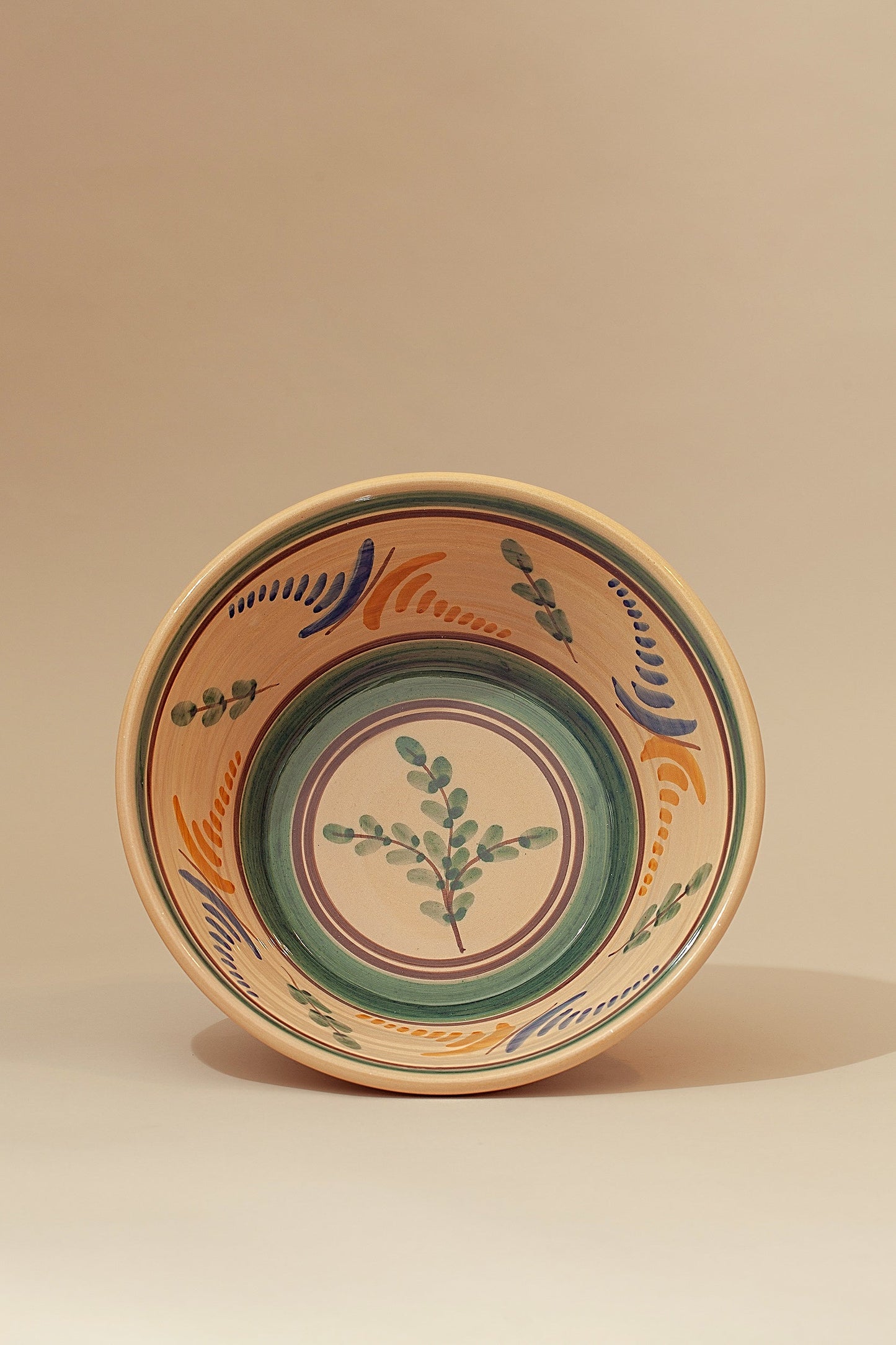 Cuenco de cerámica artesanal en tonos beige, verde y azul, decorado con un diseño floral colorido.