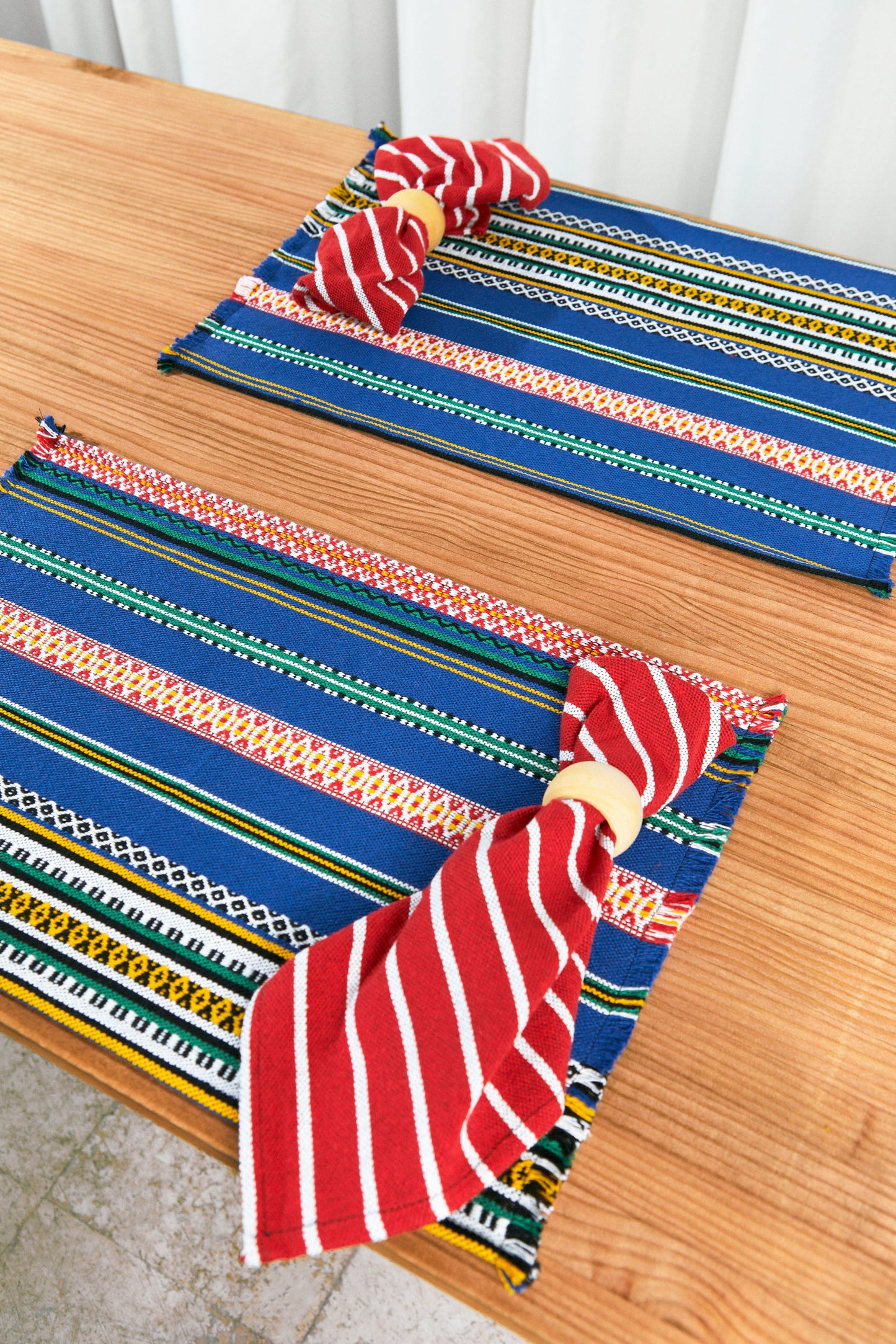 Manteles de mesa azules y rayados, tejidos de algodón, con servilletas rojas a rayas y anillos de servilleta amarillos.