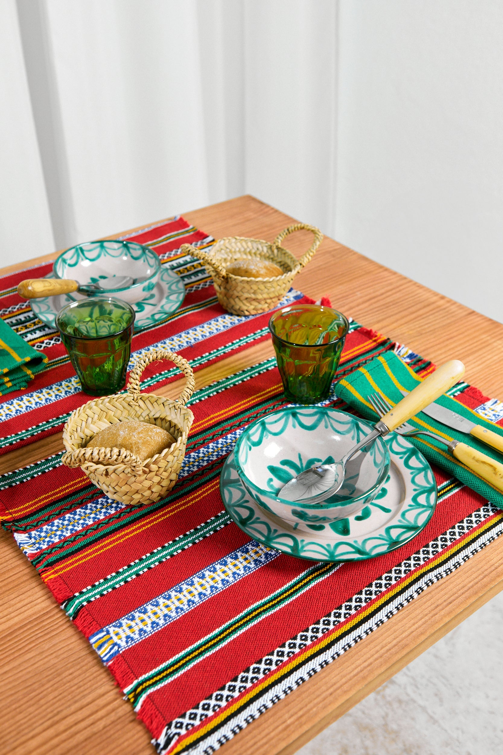 Juego de mesa colorido con manteles rojos y verdes, platos de cerámica y cestas de mimbre. Perfecto para cenas.
