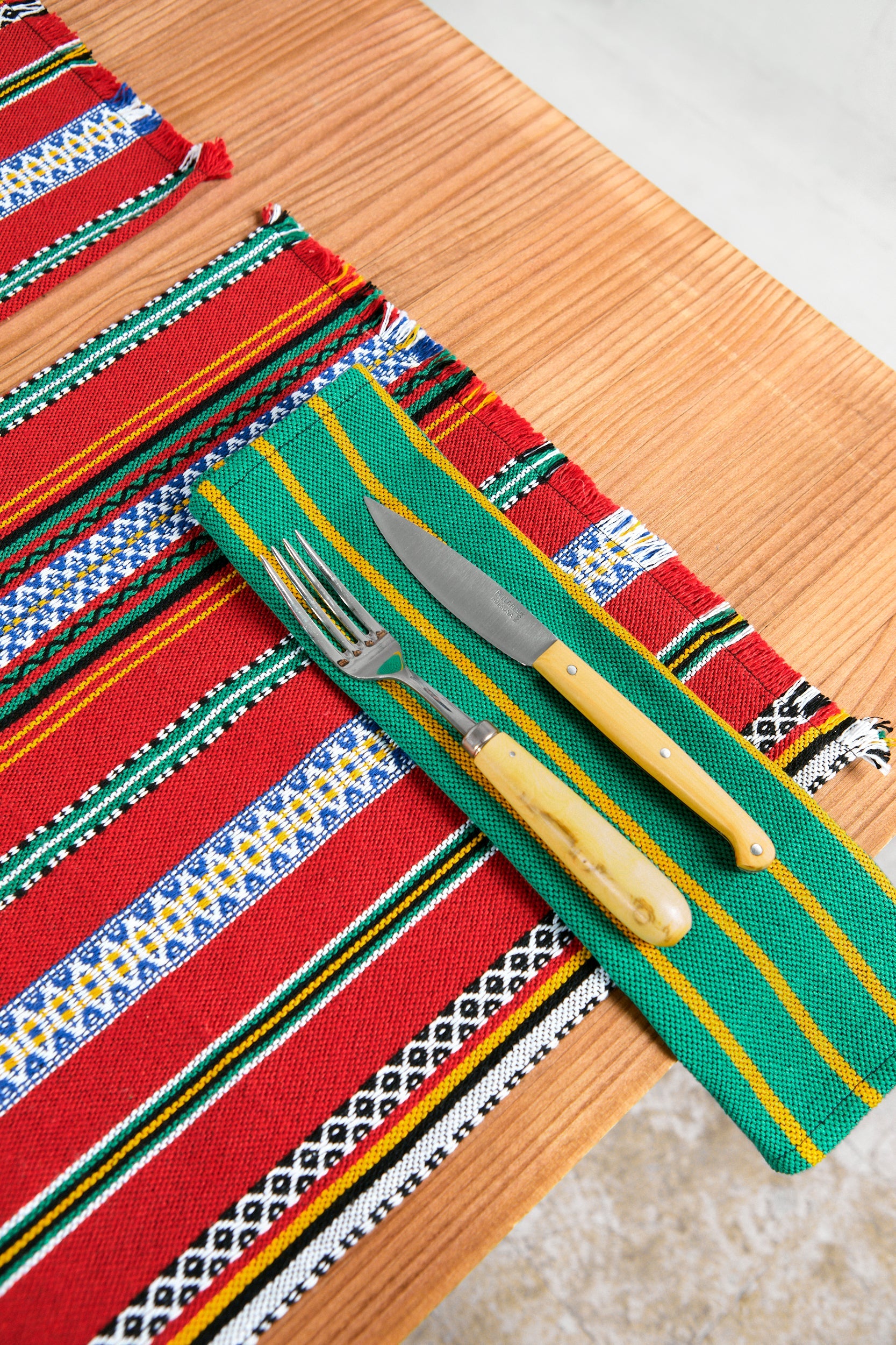 Mantel de mesa colorido en rojo y verde, tejido de algodón, con cubiertos vintage de acero y mango de madera.
