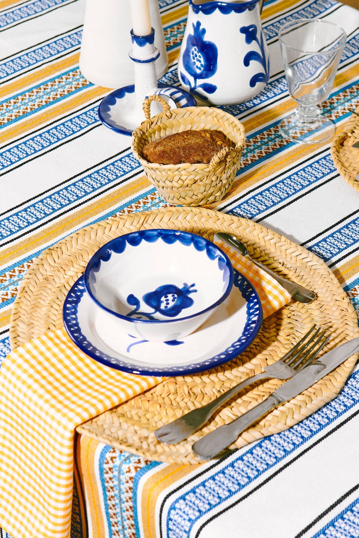 Bandeja de mimbre, juego de platos de cerámica blanca y azul, manteles con rayas amarillas y azules.