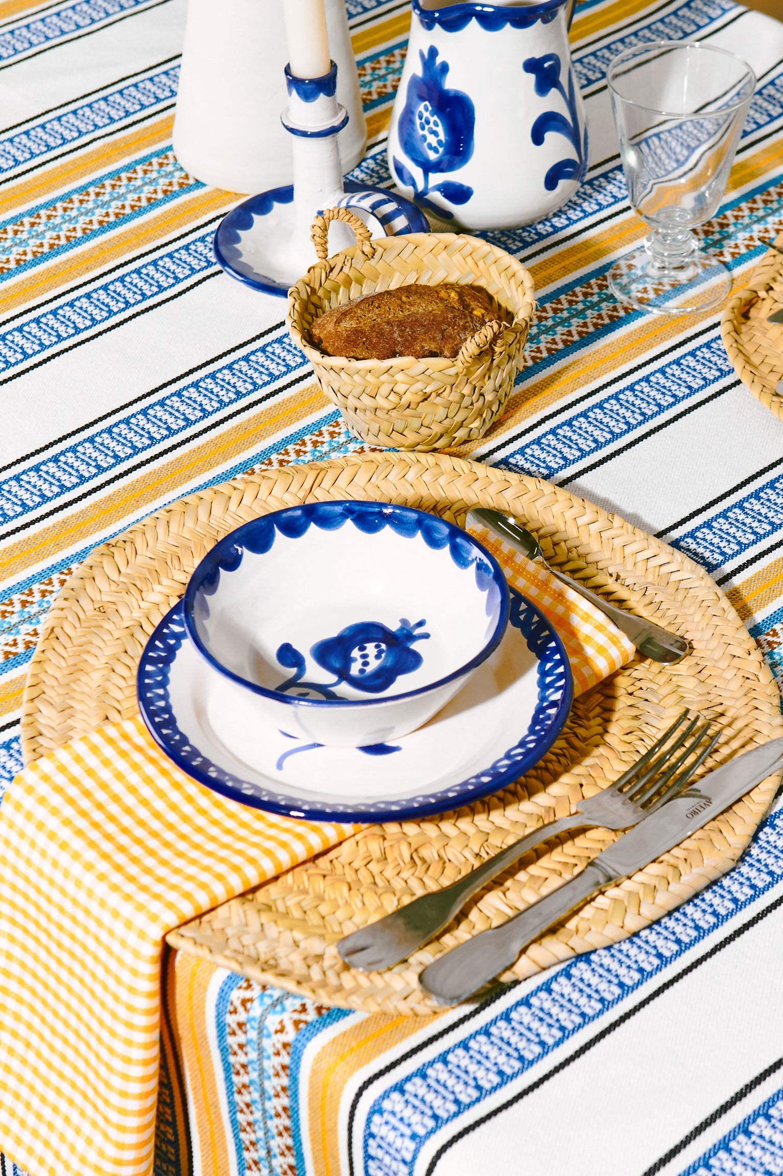 Bandeja de mimbre, juego de platos de cerámica blanca y azul, manteles con rayas amarillas y azules.
