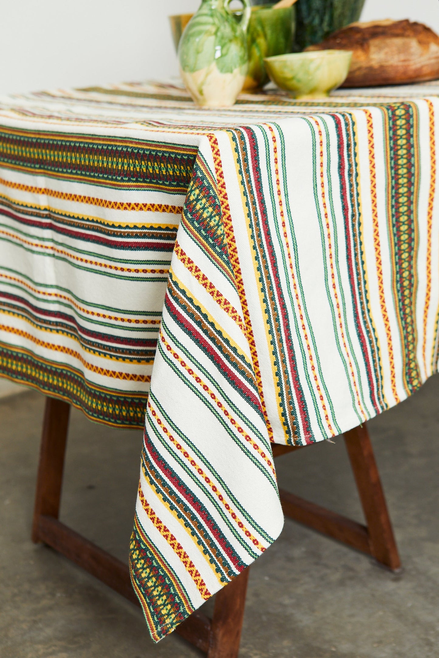 Mantel de algodón blanco con rayas en verde, rojo y amarillo; estilo bohemio y texturizado, ideal para decoración.