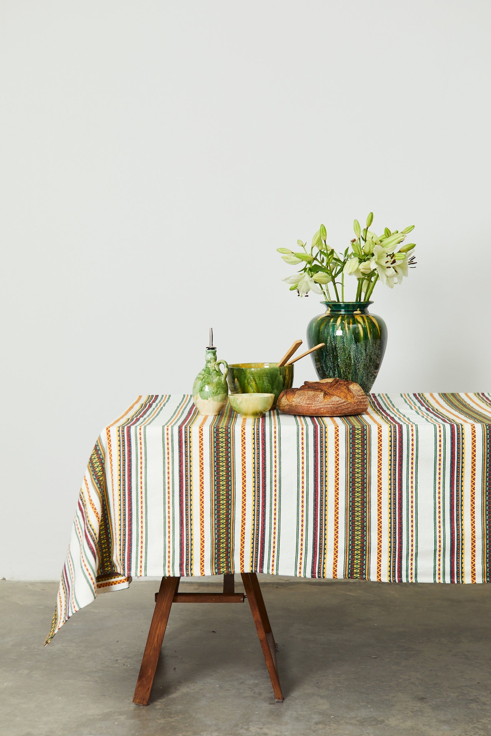 Mantel de rayas multicolor en tonos terracota y verde, algodón, estilo rústico, sobre mesa de madera con decoraciones.
