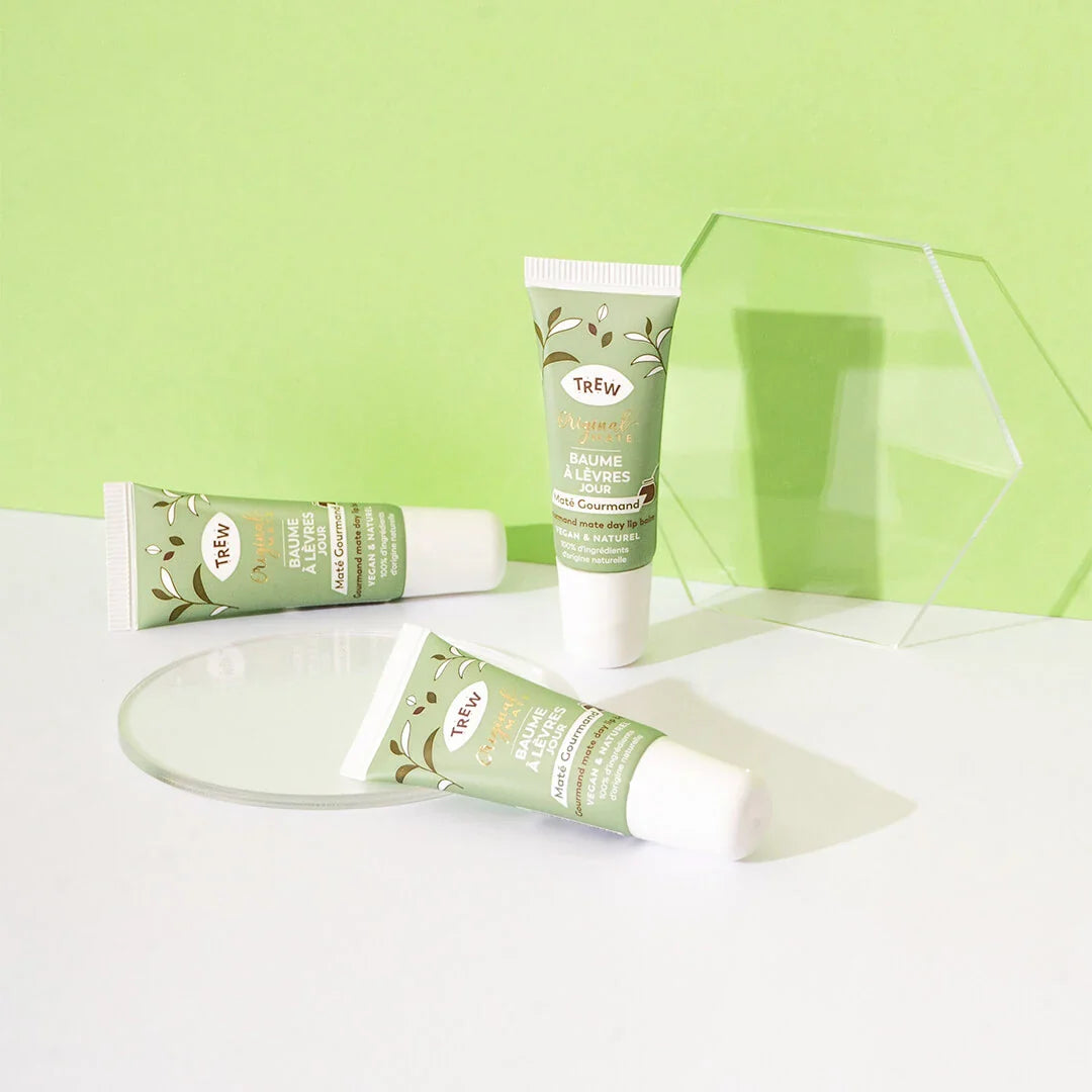 Three tubes of Trew lip balm in pale green packaging with botanical motifs, displayed on clear acrylic stands.
