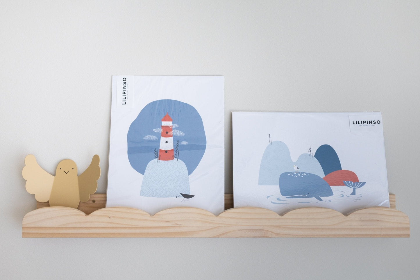 Imágenes de arte en colores azul y rojo con un faro y montañas, en marco de madera claro. Ideal para decoración infantil.