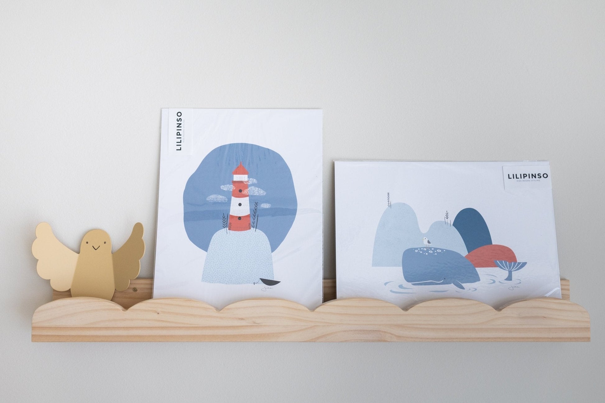 Imágenes de arte en colores azul y rojo con un faro y montañas, en marco de madera claro. Ideal para decoración infantil.