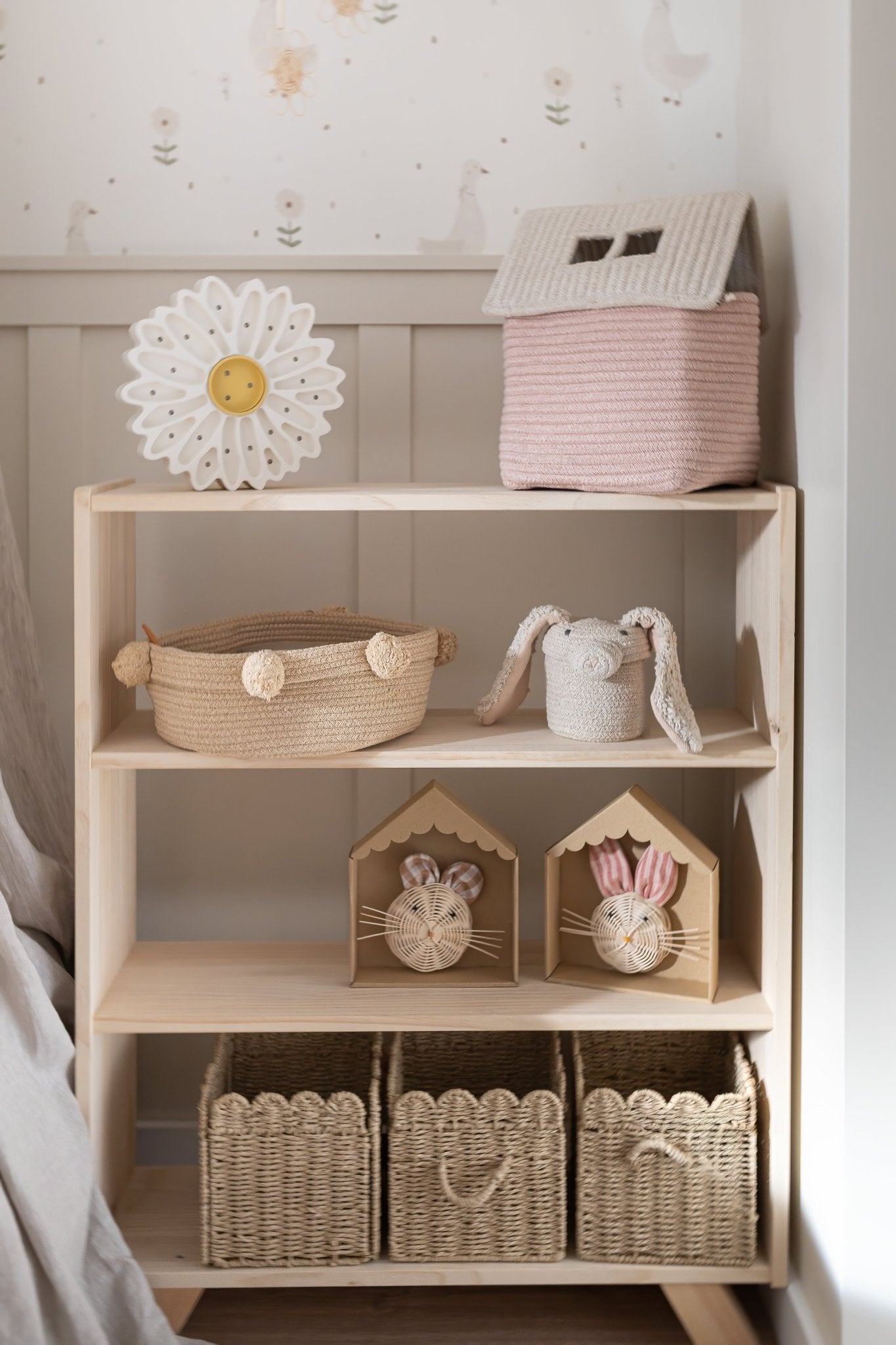 Estantería de madera clara con decoración en tonos rosa y natural, cestas tejidas y adornos de conejitos.