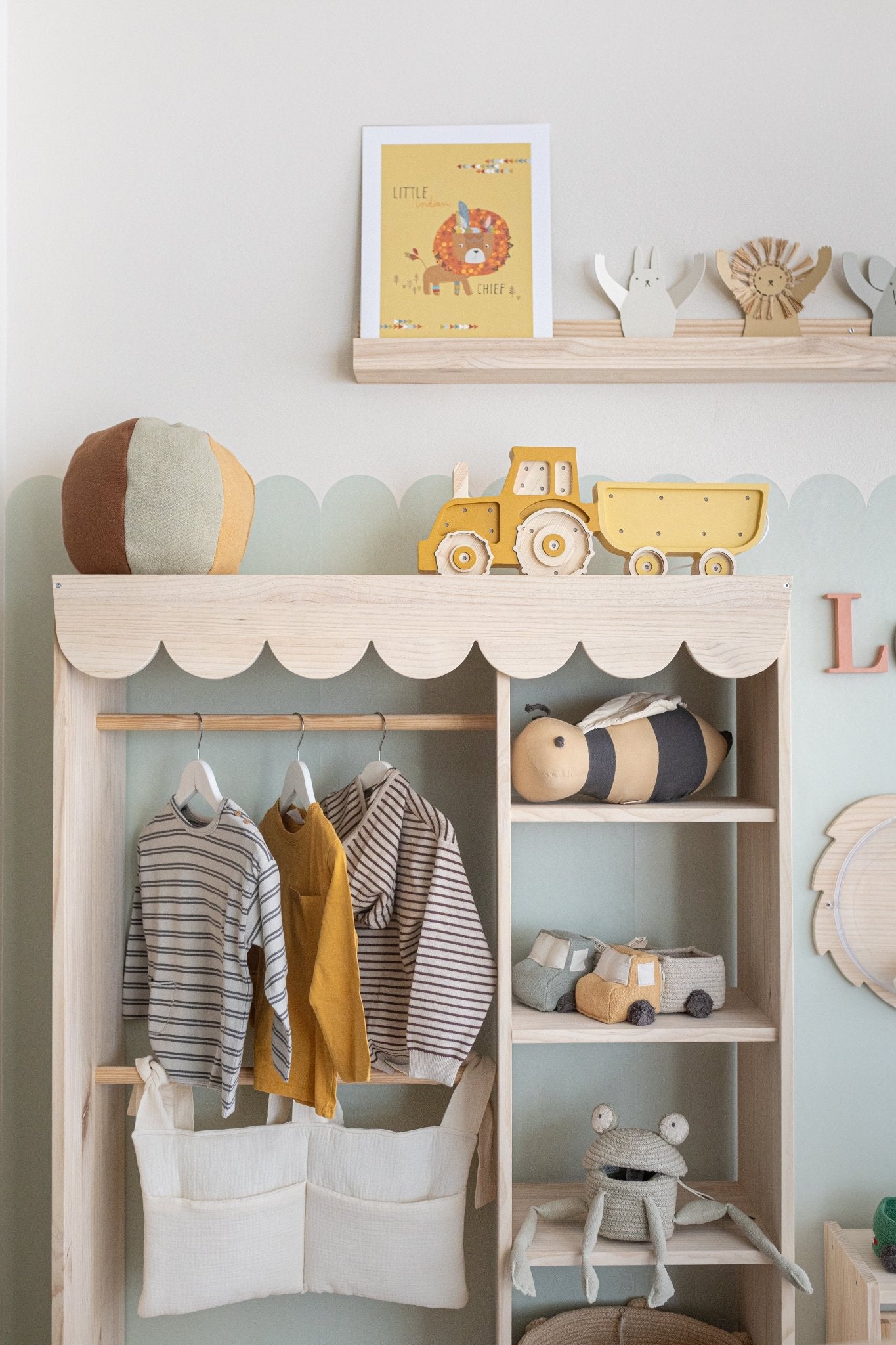 Ropa infantil en tonos amarillos y rayas, organizadores de tela y juguetes de madera en un mueble acogedor de madera.