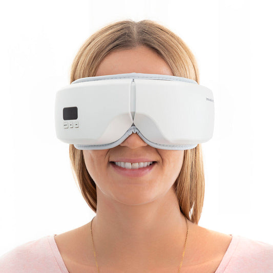 Mujer sonriendo usando un masajeador de ojos blanco, ergonómico y moderno, con panel de control integrado.