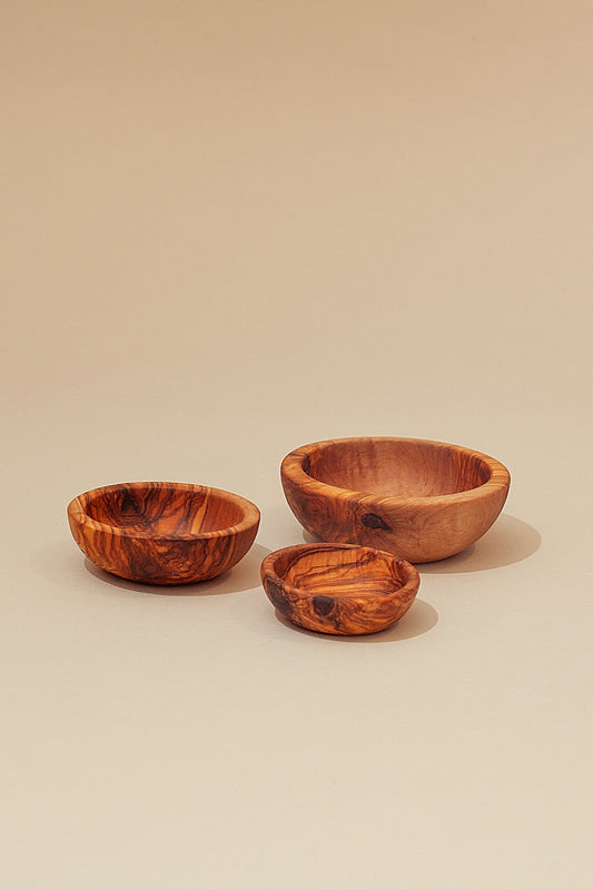 Set de tres cuencos artesanales de madera de olivo con veteado natural, sobre fondo beige neutro.