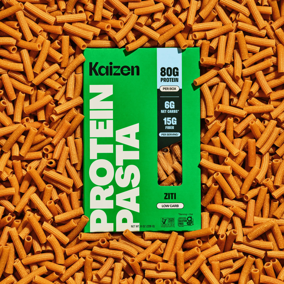 Kaizen Protein Pasta Ziti box on a bed of dry, tubular, brown-colored ziti pasta noodles.