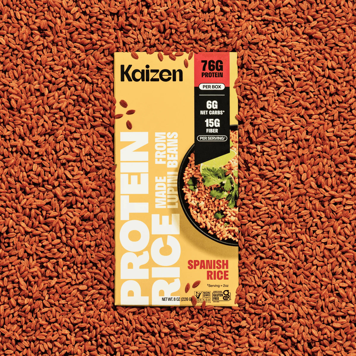 Yellow box of Kaizen Protein Spanish Rice centered on a background of loose, cooked reddish-brown rice grains.