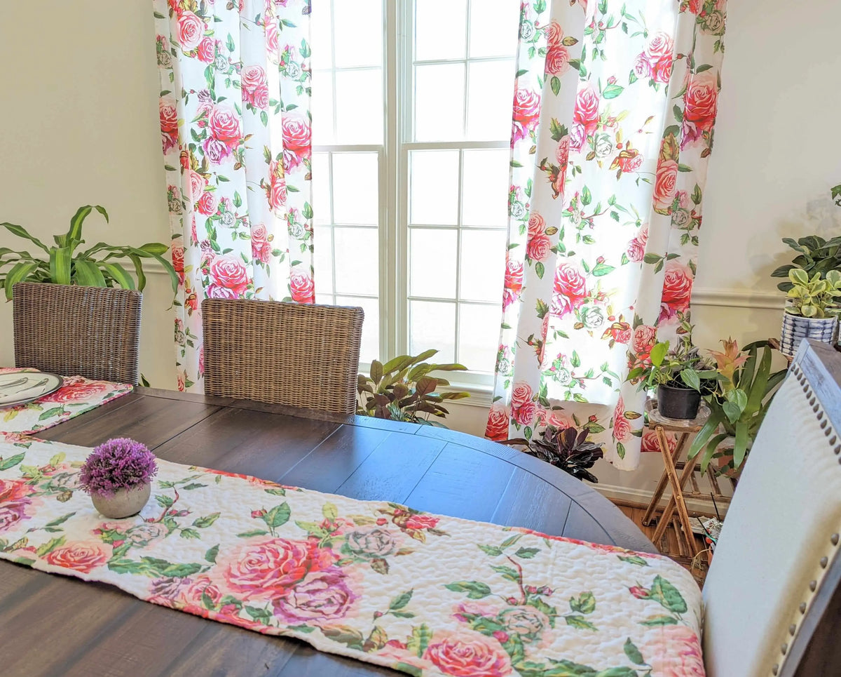 Quilted dining table runner with a romantic pink and white rose floral print on a dark wooden table.