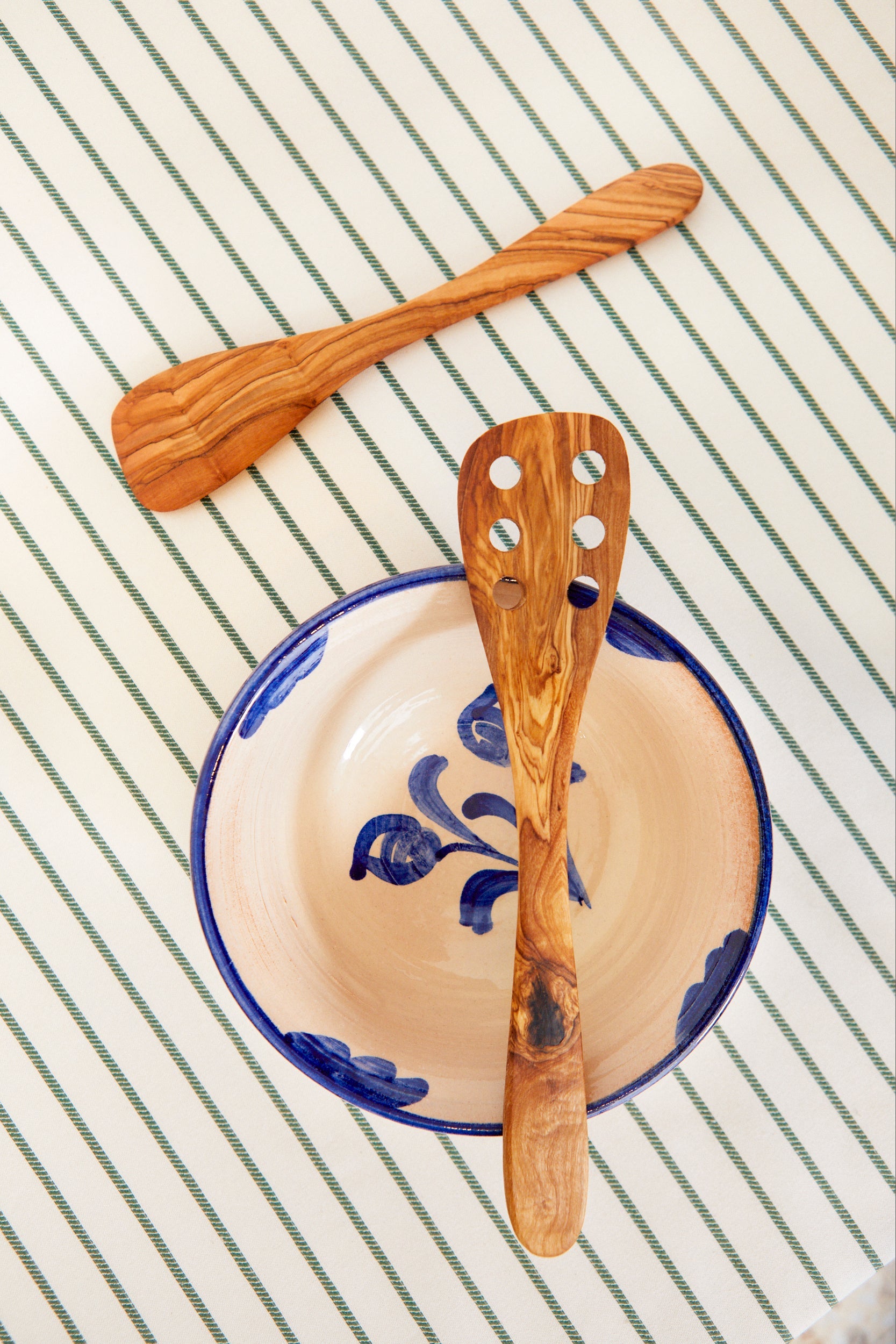 Cuenco cerámico beige con detalles azules y cucharón de madera de olivo sobre fondo de tela rayada.