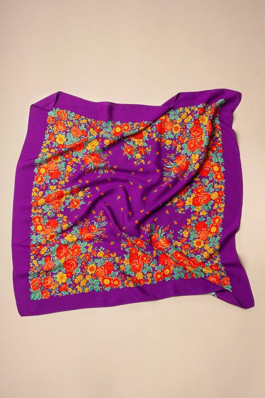 Pañuelo cuadrado de tela morada con estampado tradicional de flores rojas, naranjas y amarillas sobre fondo beige.